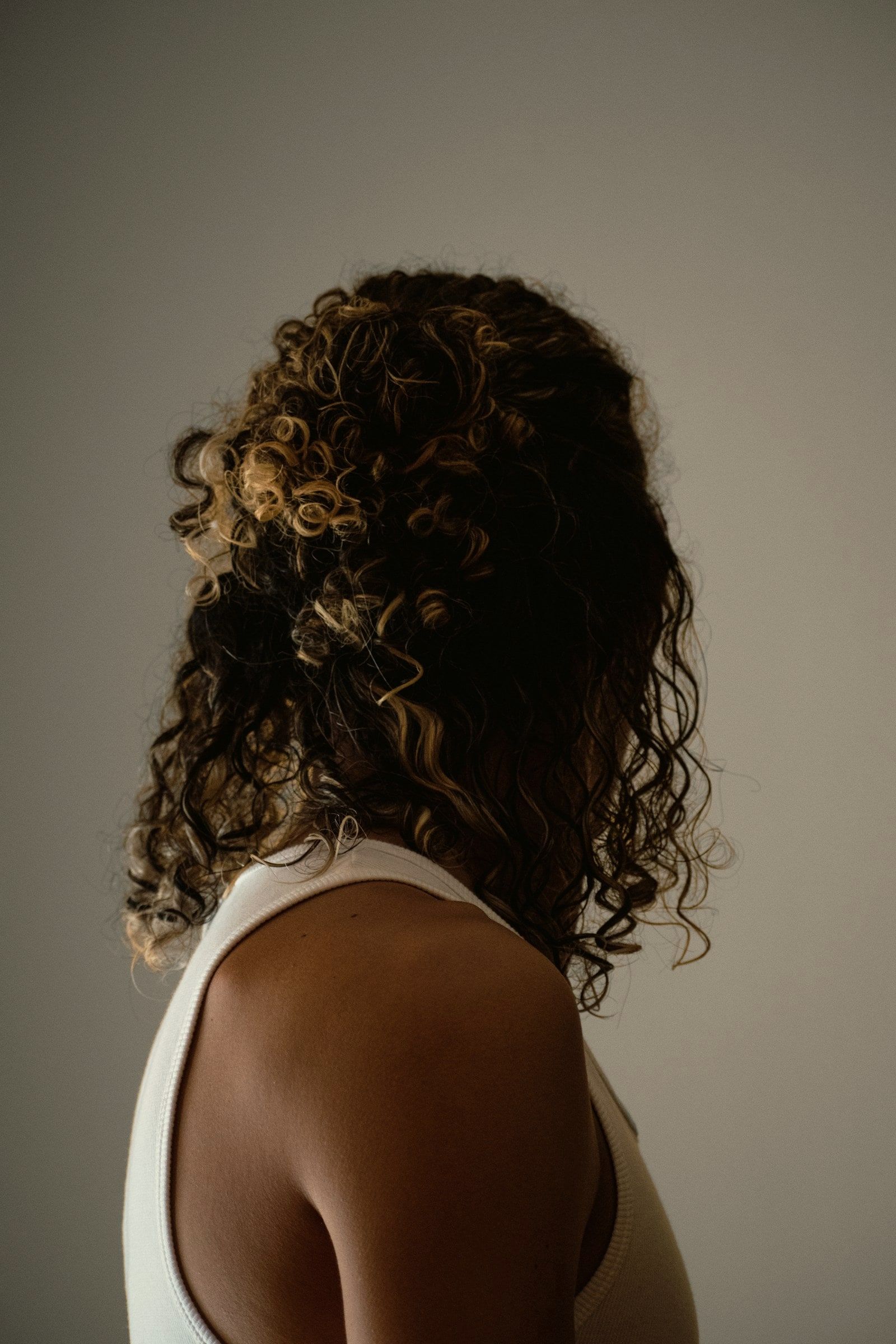 Natürliche dunkle Locken mit hellen Spitzen, in Form geschnitten, von hinten